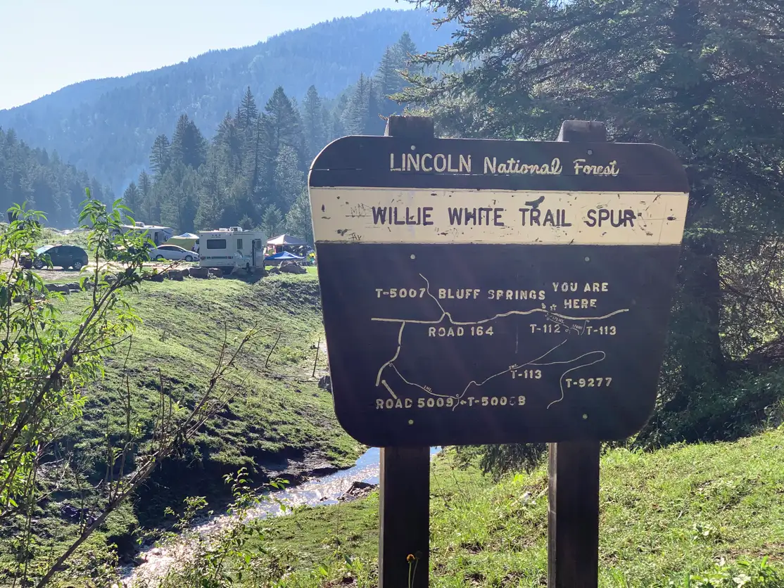 Lincoln National Forest Willie White Trail Spur sign with trail map, RVs and green meadow in background