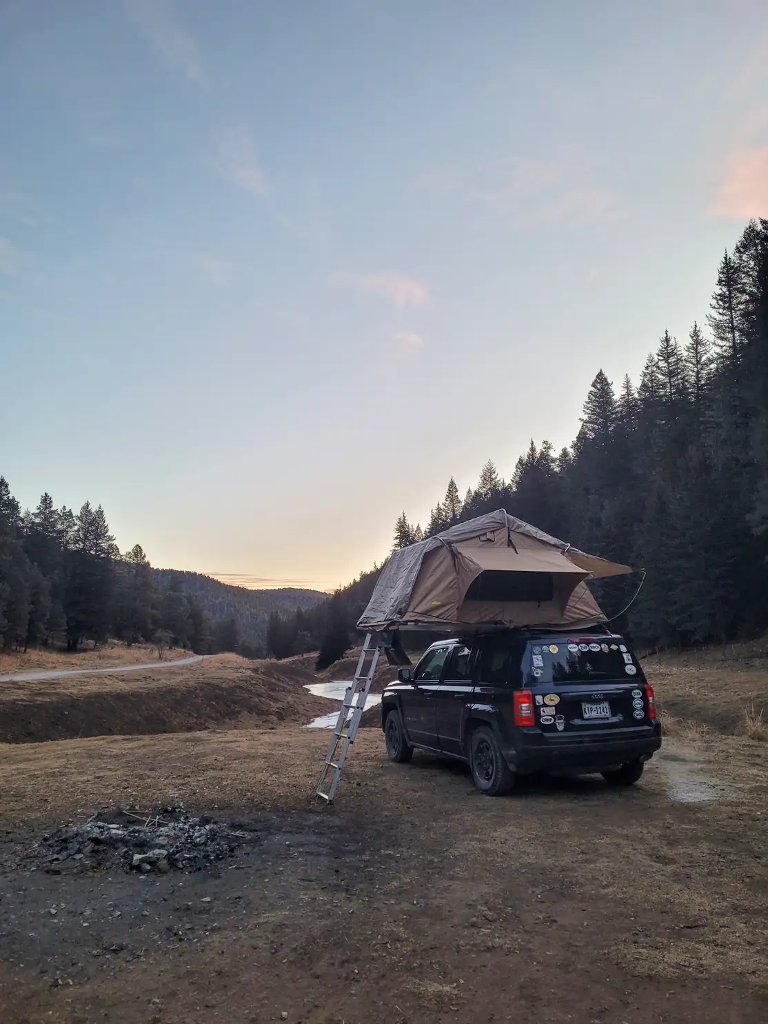 Rooftop tent deployed on an SUV at a dispersed site at dusk with mountain forest in the background