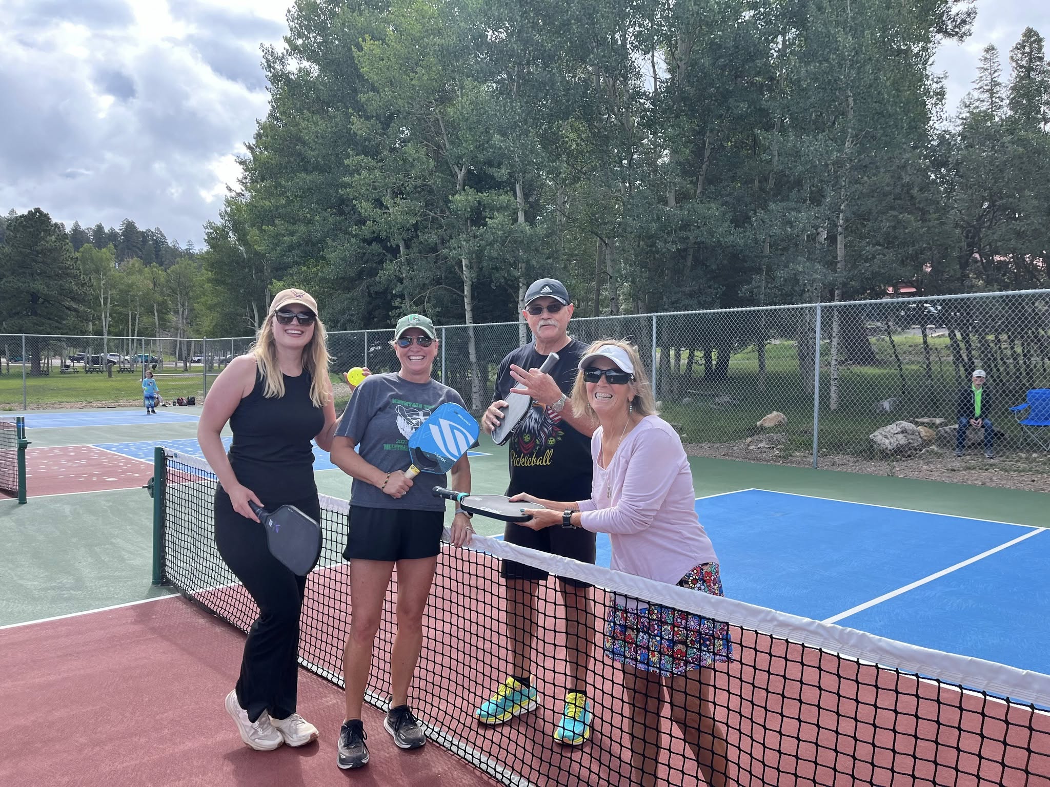 Four players posing at the net with paddles raised, aspen and pine trees behind them