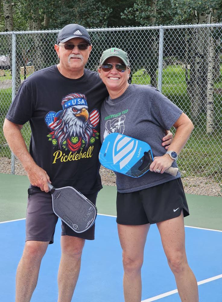 Couple posing courtside with paddles, man wearing USA Pickleball shirt