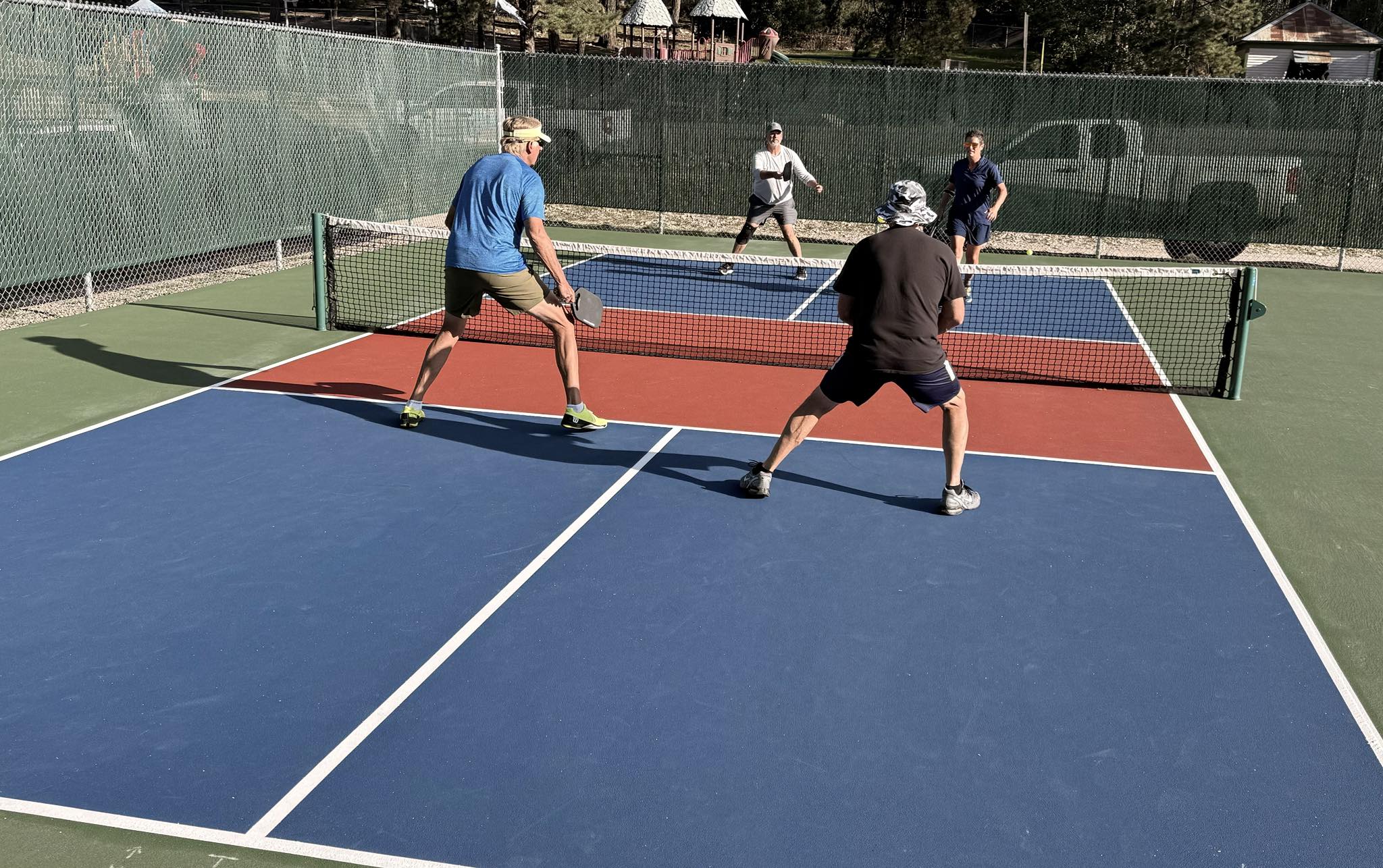 Four players in a competitive doubles rally on the blue and red Zenith Park courts