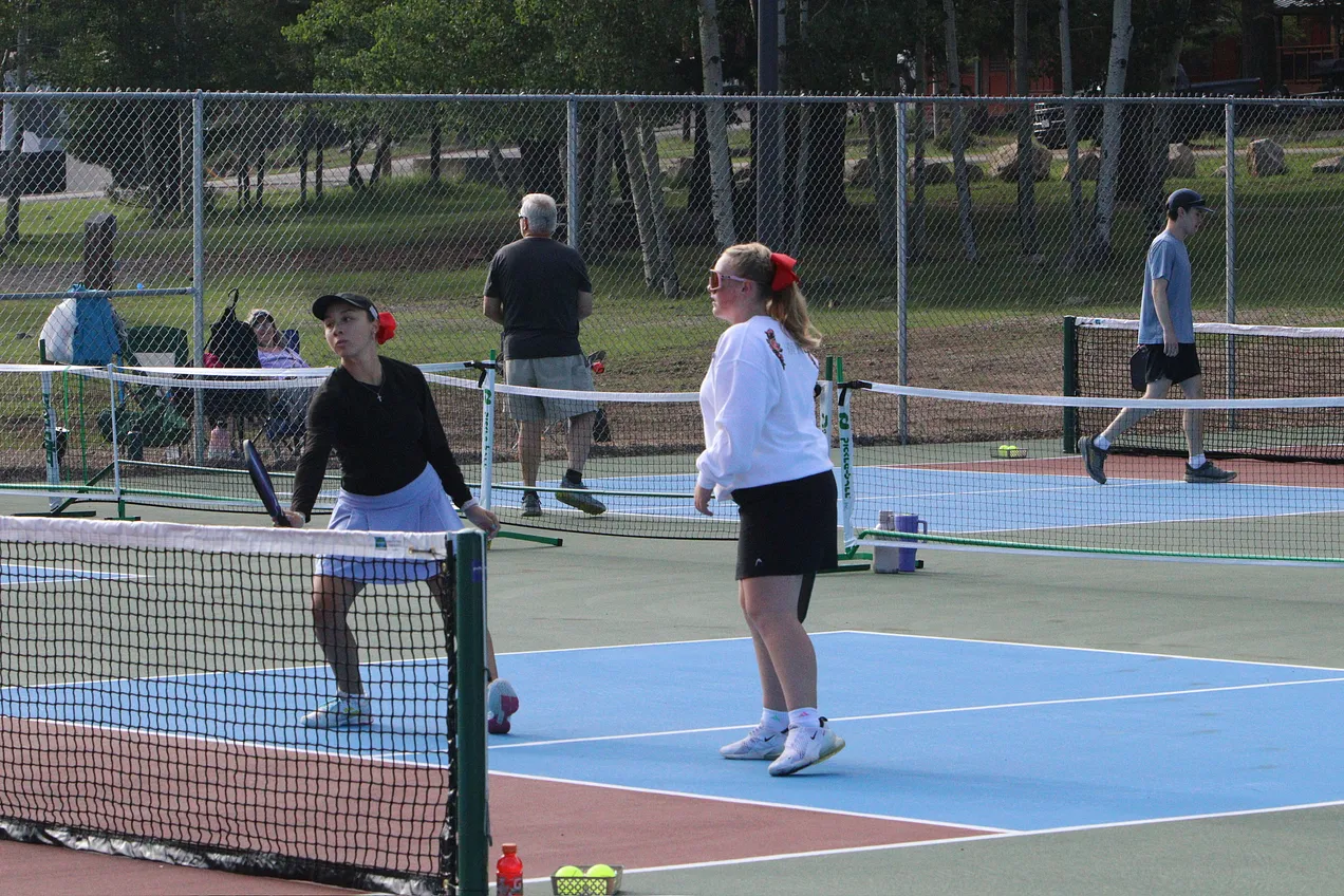 Women playing doubles on Zenith Park courts with multiple courts active in the background