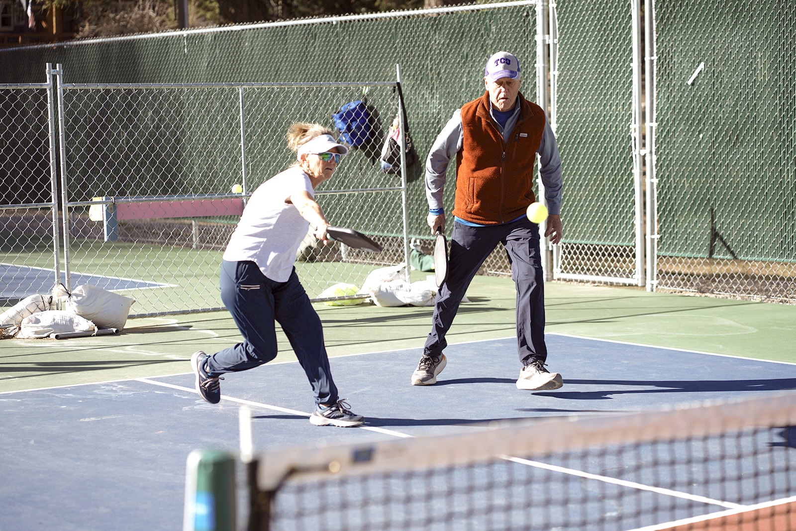 Mixed doubles partners in action, woman lunging for a volley at the kitchen line