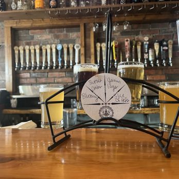 Four-pour beer flight on a wooden carrier with a hand-written tasting card