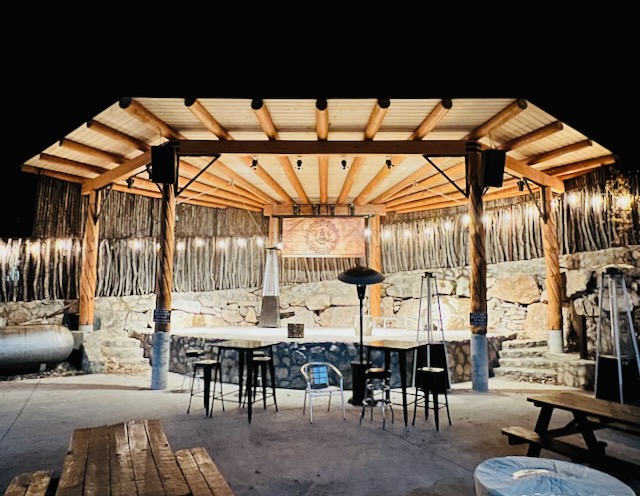 Covered outdoor stage and bar tables at night, lit by string lights and patio heaters