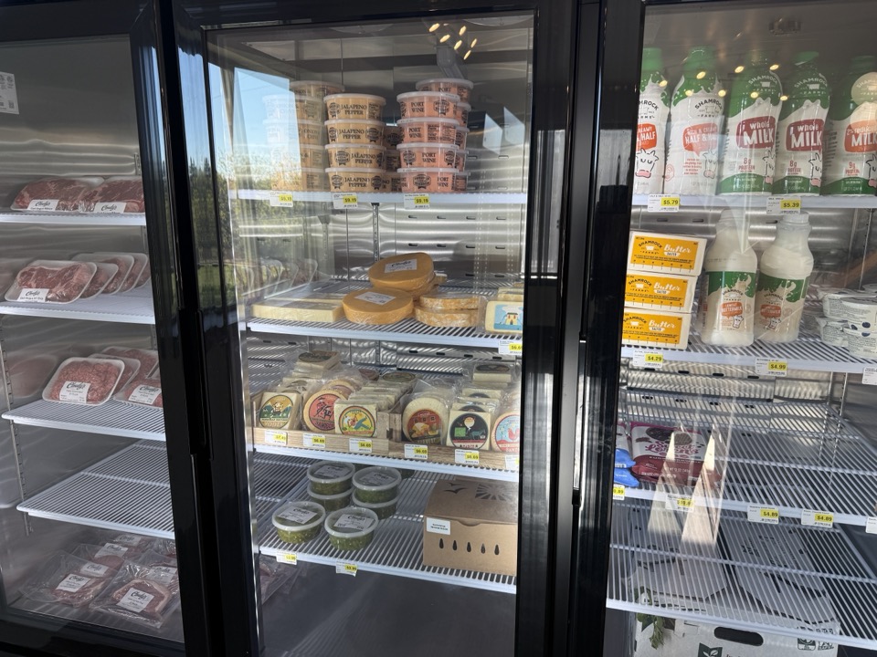 Glass-front refrigerated case at Cloudy's Market stocked with packaged meat, butter, cheeses, salsas, and bottled whole milk