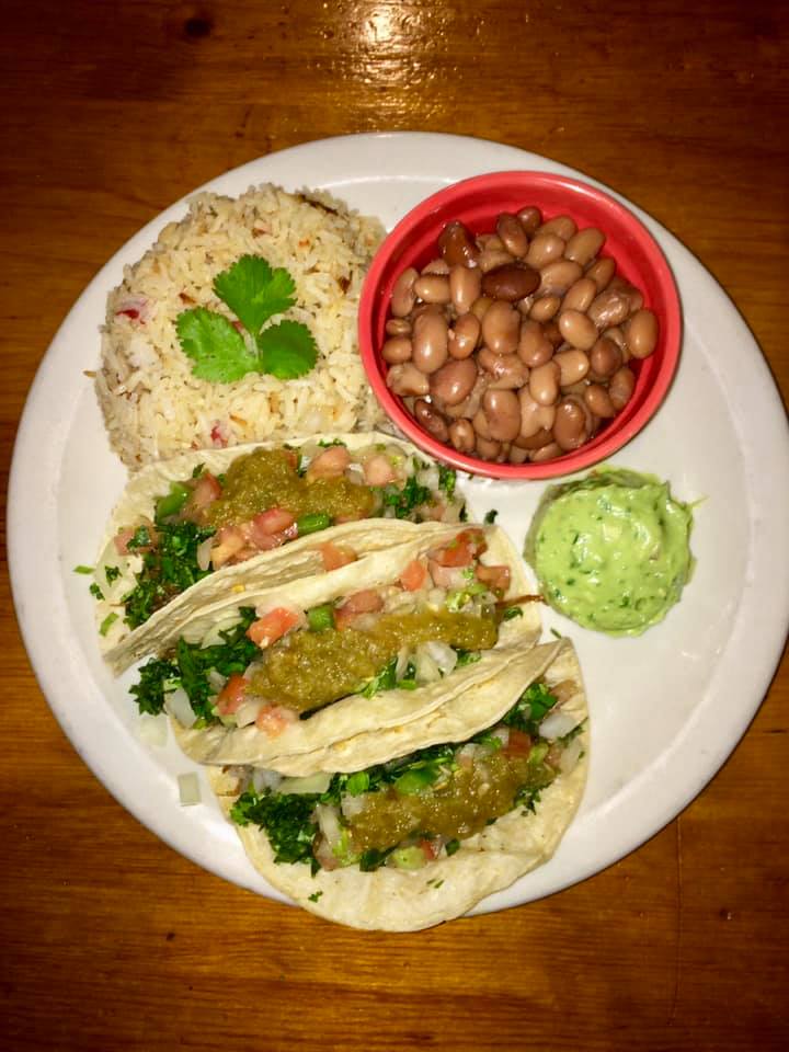 Three street-style tacos with cilantro, onion, and salsa verde, served with rice, pinto beans, and guacamole