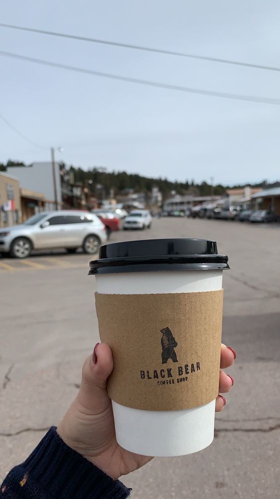 Black Bear cup held up with downtown Cloudcroft in the background