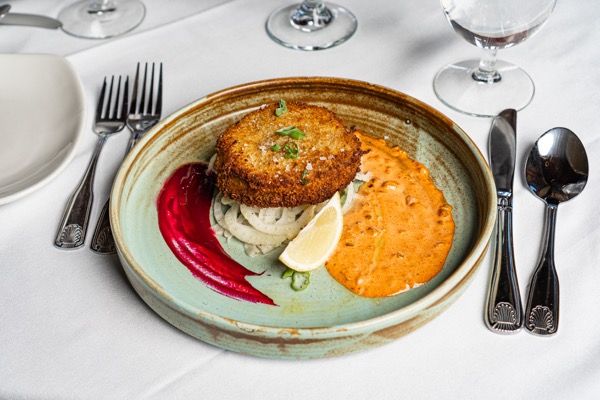 Crab cake with beet and pepper sauces on a handmade ceramic plate at Eighteen99