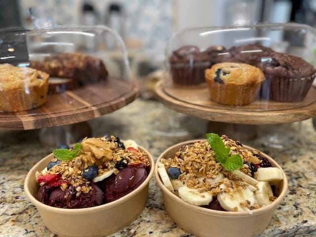 Acai bowls topped with granola, fresh fruit, and mint alongside house-baked muffins