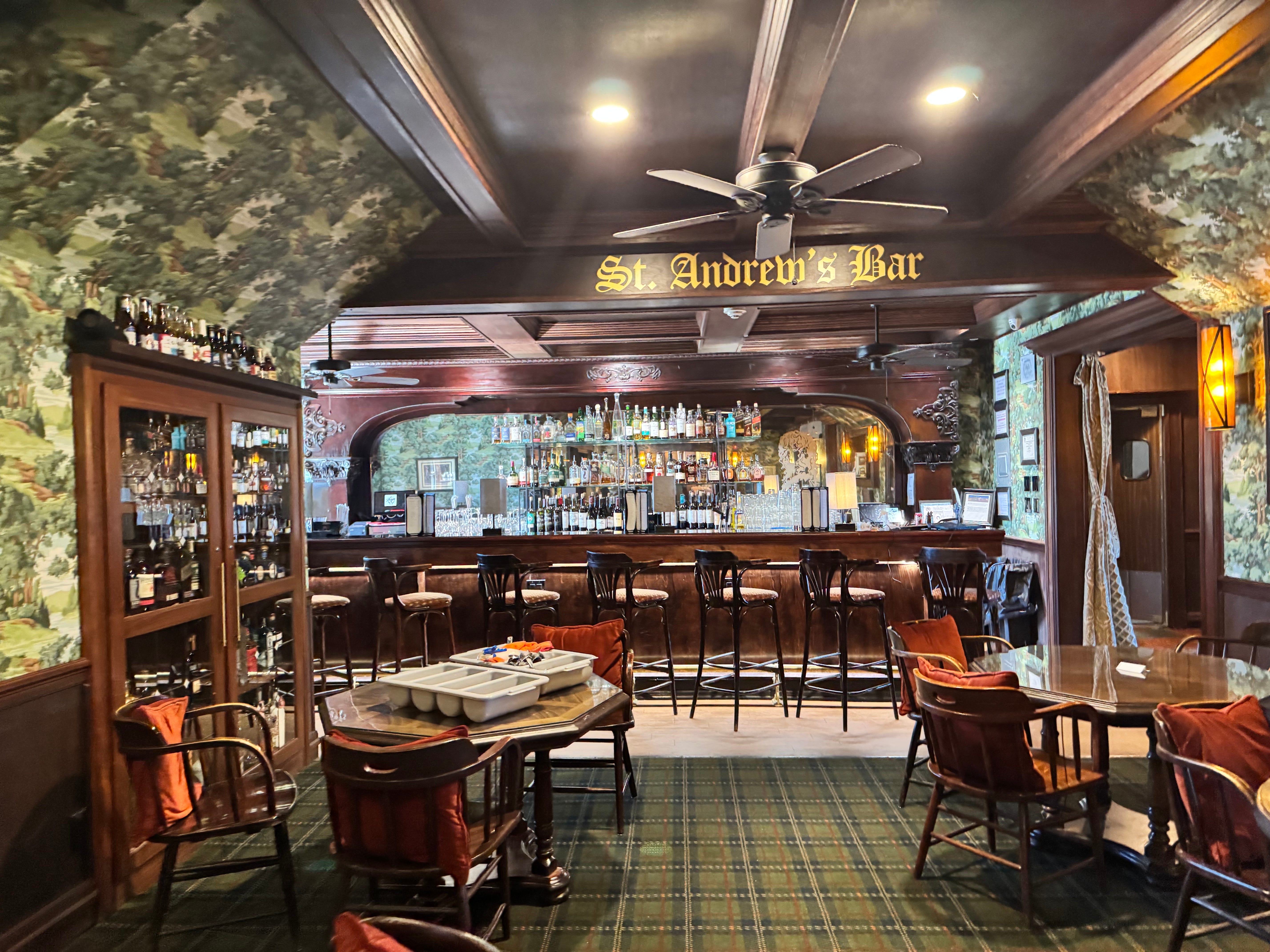 Full interior of St. Andrew's Bar with dark wood bar, stools, and St. Andrew's Bar sign overhead