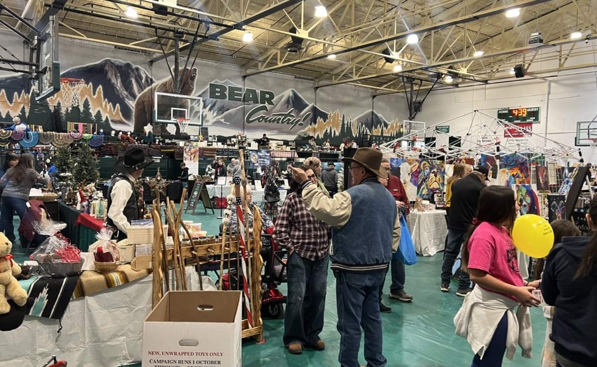 Shoppers browsing vendor booths under the Bear Country mural at the Cloudcroft Christmas Market