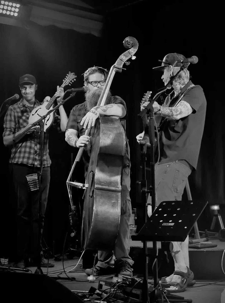 Black-and-white photo of a four-piece band on stage with upright bass, guitars and mandolin at Cloudcroft Brewing Company