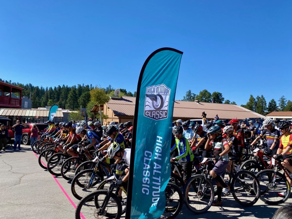 Riders lined up at the start of the High Altitude Classic in downtown Cloudcroft with the branded feathered banner