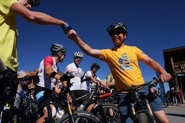 Fist bump between racers at the start, one in a yellow Oak Flats jersey