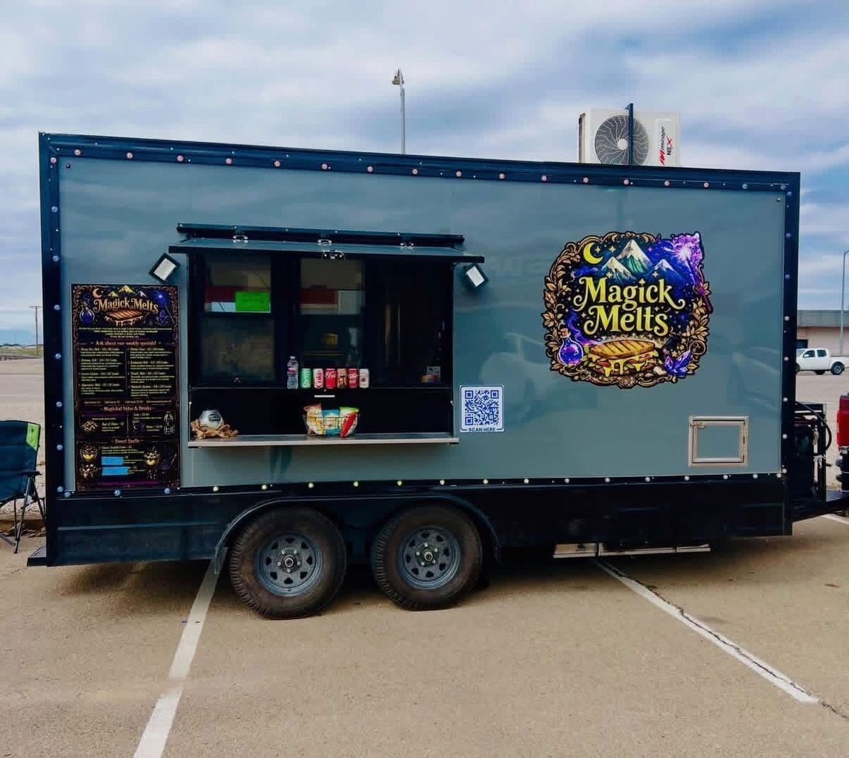 The Magick Melts food truck, a gray trailer with a mountain-and-moon logo and a serving window, parked in a lot