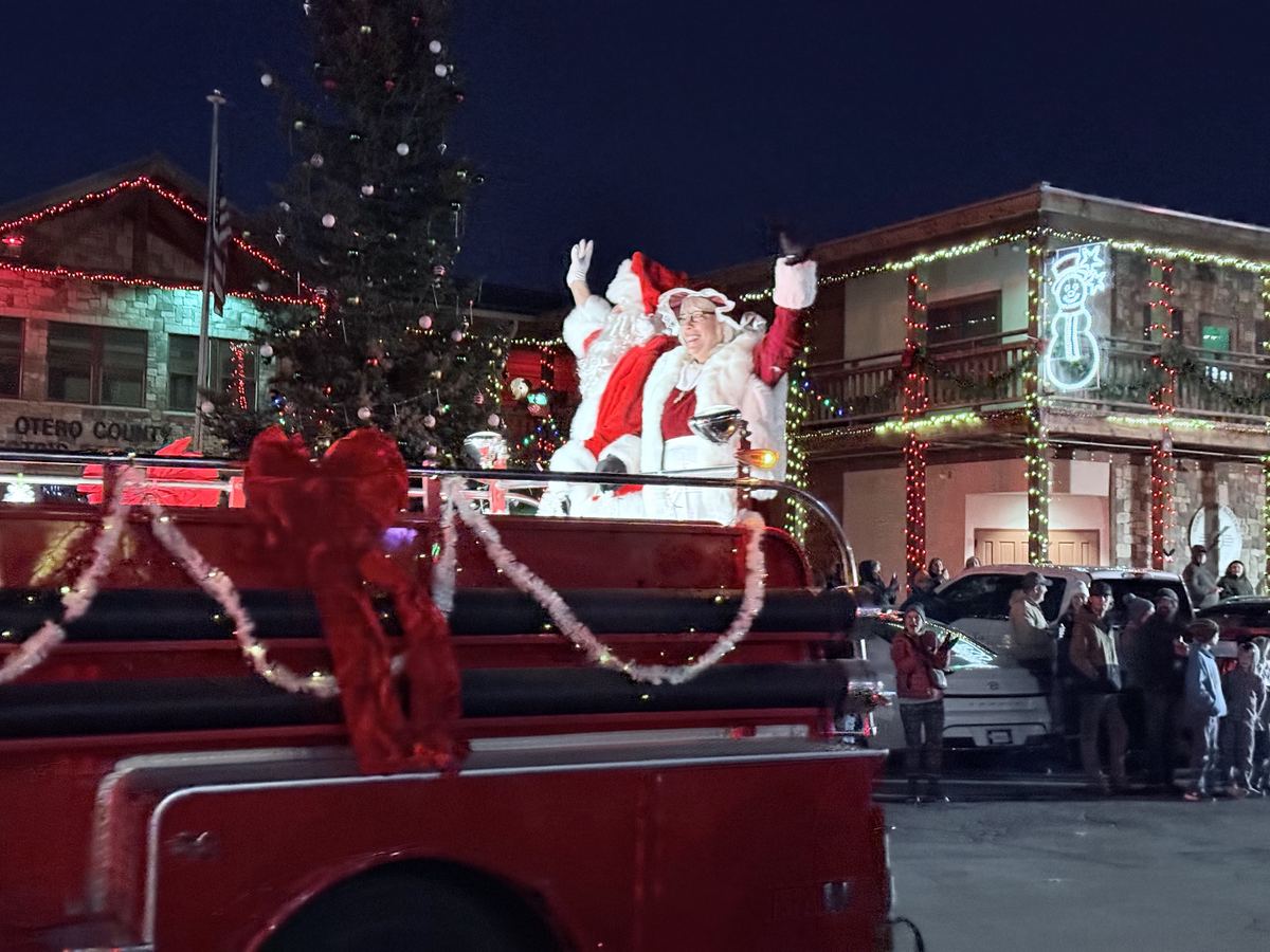 Santa and Mrs. Claus waving from a vintage red fire truck beside the lit Christmas tree in downtown Cloudcroft