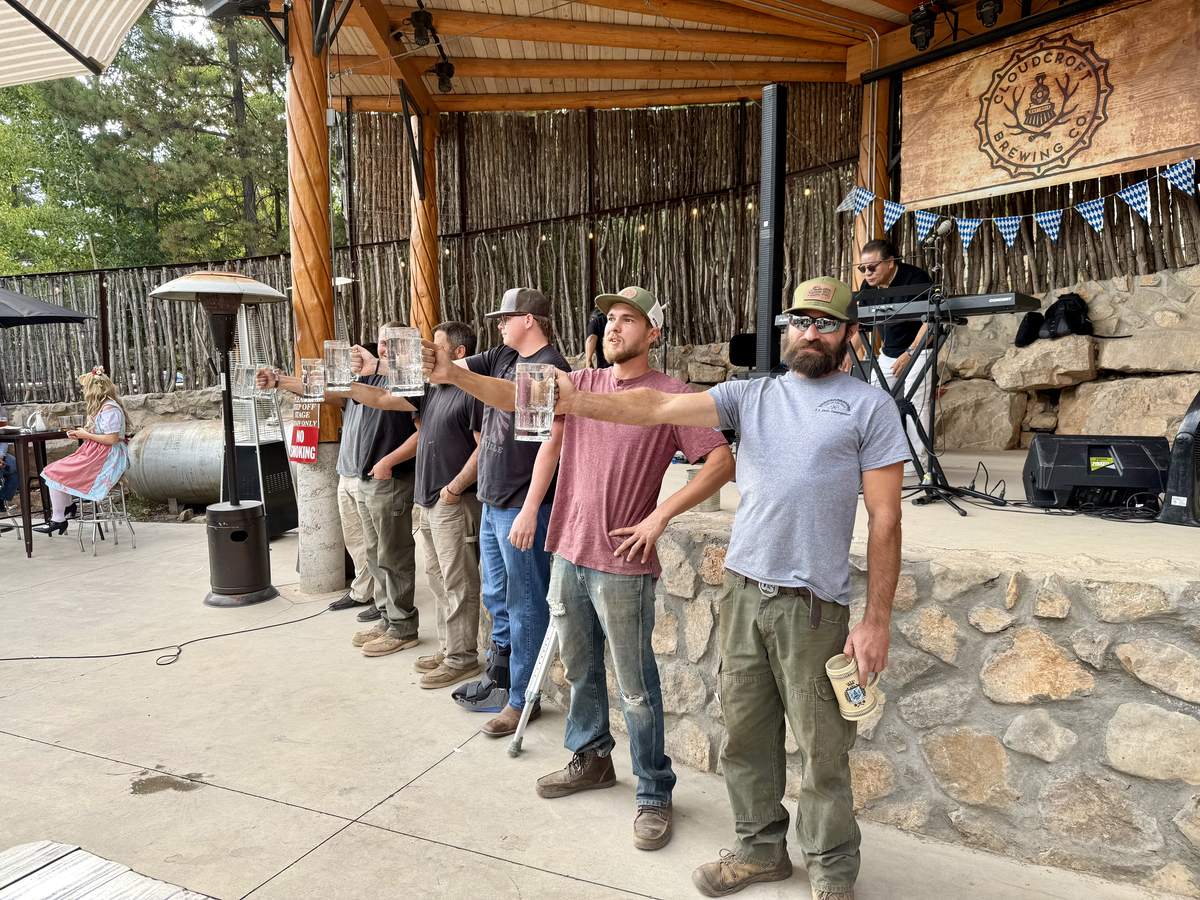 Competitors holding beer steins at arm's length during the stein-holding competition on the Cloudcroft Brewing Company patio