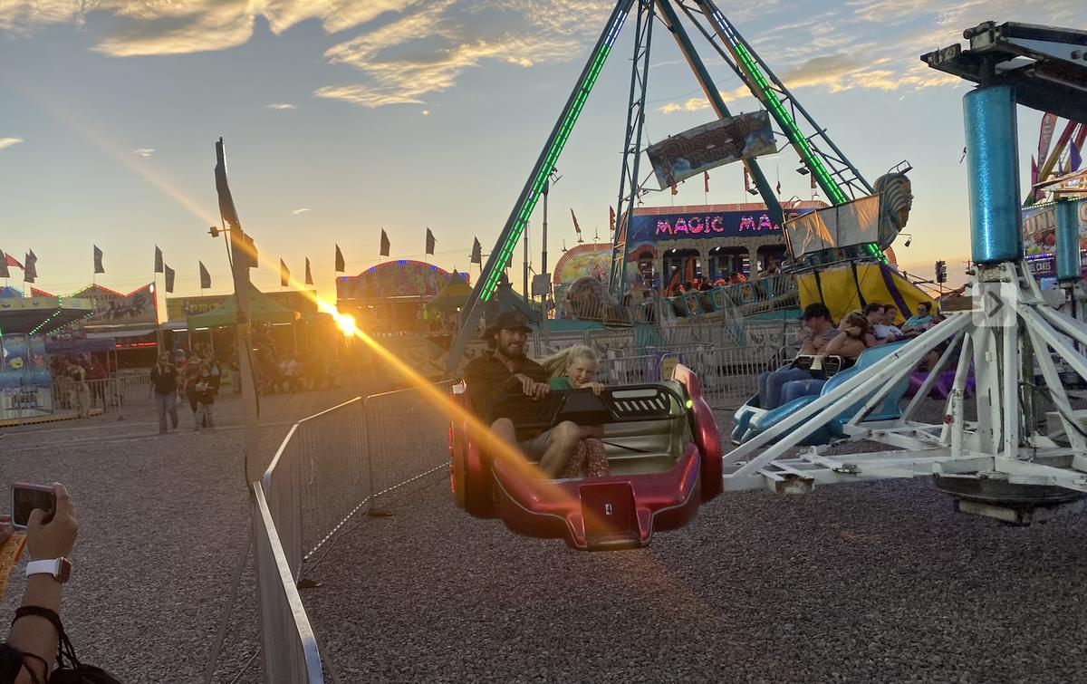 Fair-goers on a spinning carnival ride at sunset on the midway at the Otero County Fair