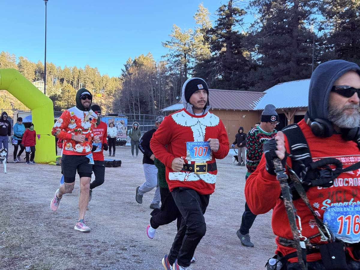 Runners in Santa suits and holiday sweaters heading out from the start of the Cloudcroft Ugly Sweater 5K