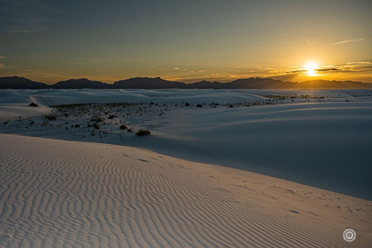 Rippled white gypsum dunes at White Sands National Park with the sun setting behind the mountains