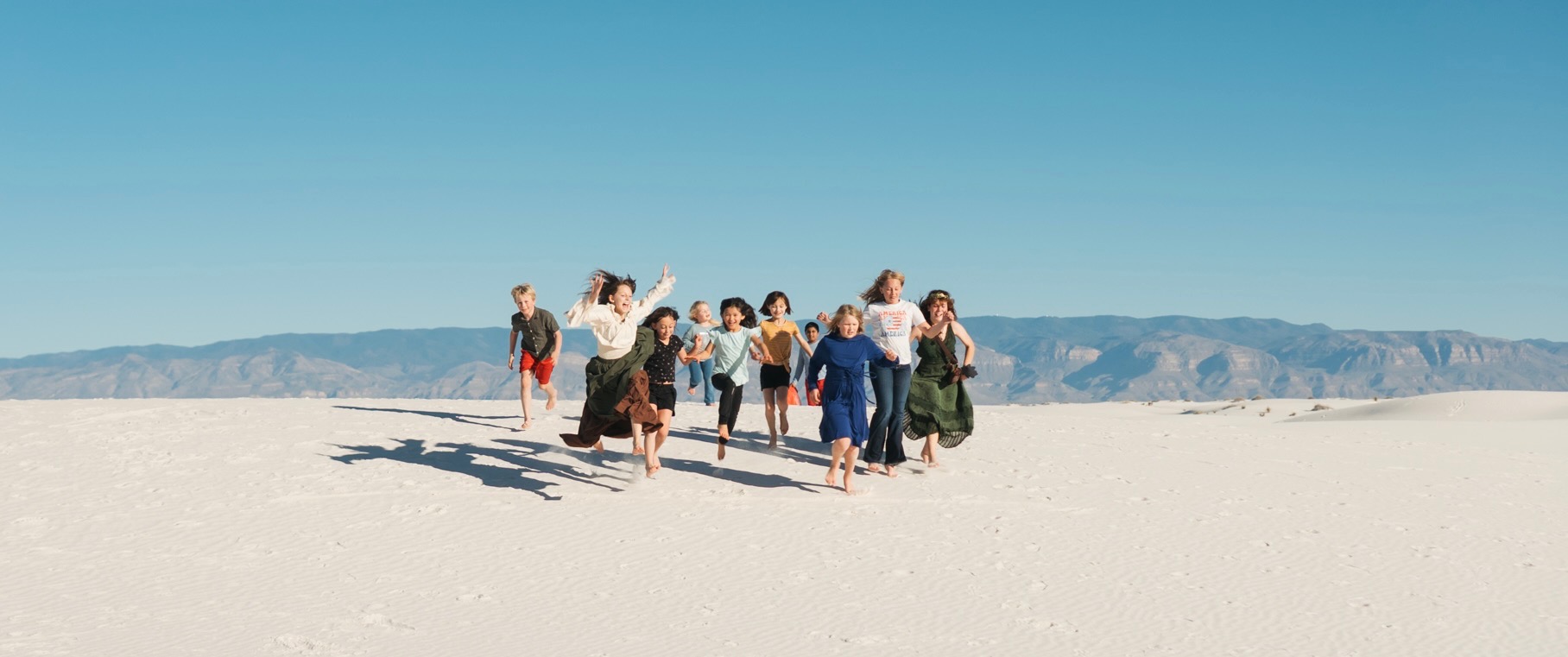 A group of children running barefoot across the white gypsum dunes at White Sands National Park near Alamogordo, New Mexico