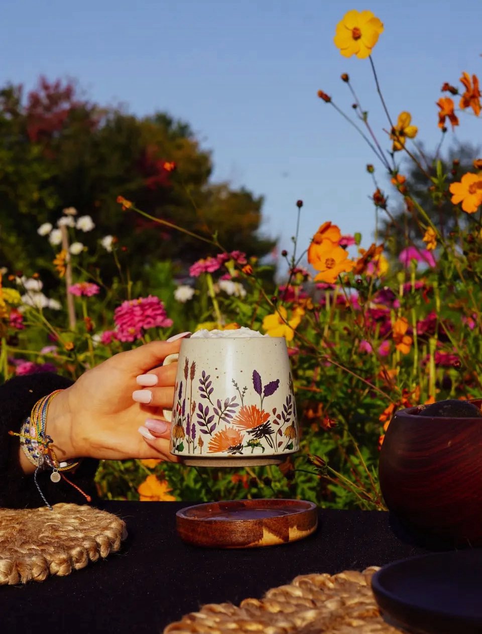 Hand holding a wildflower-pattern ceramic mug in a flower garden at golden hour