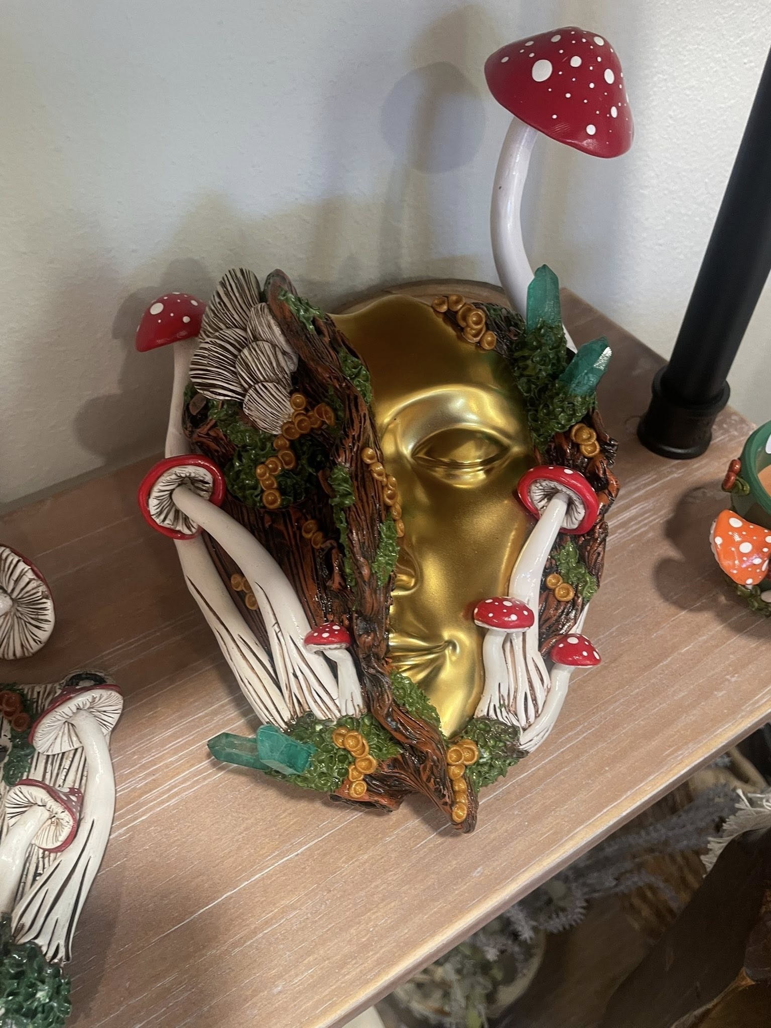 Gold face mask sculpture with red-capped mushrooms and crystal accents