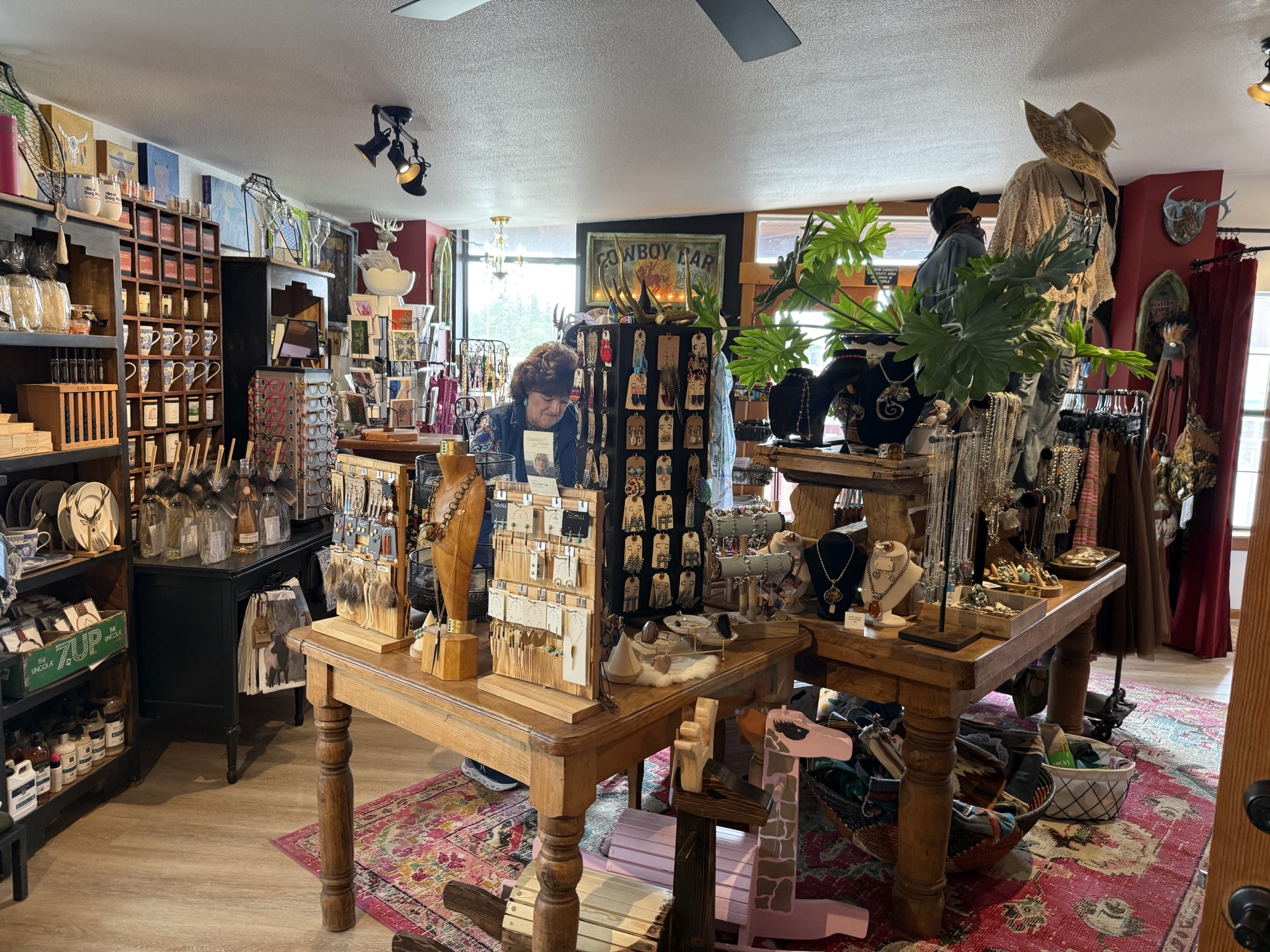 Wide interior at The Elk Shed showing wooden jewelry tables with turquoise displays, a hat-wearing mannequin, framed Cowboy Land art, and a pink-and-green Christmas tree against a wood-paneled wall