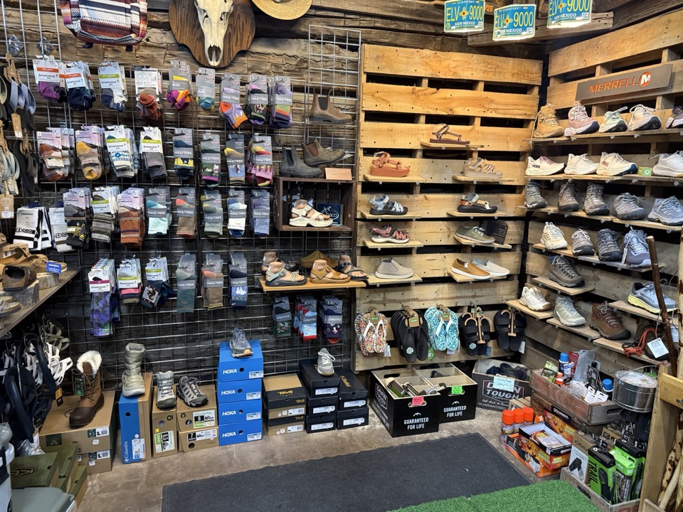 Footwear wall at High Altitude with Hoka, Merrell, and hiking boots on pallet shelves and a sock display