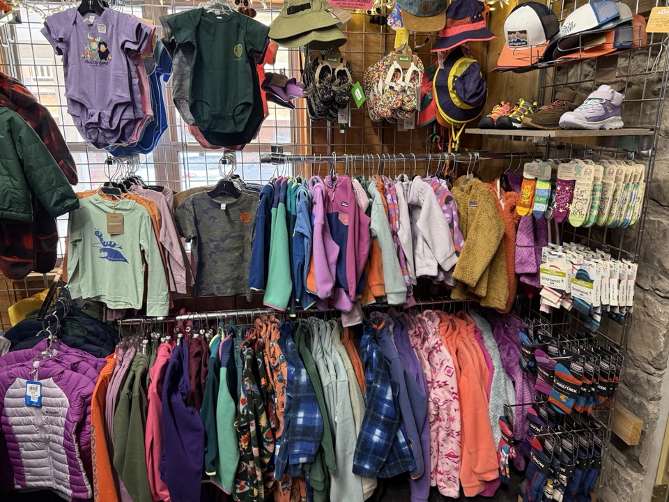 Kids and youth clothing rack at High Altitude with onesies, fleece jackets, hoodies, and small puffer coats