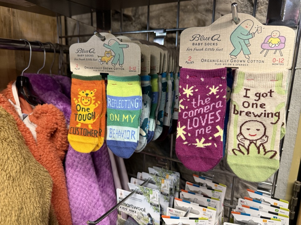 Blue Q novelty baby sock display at High Altitude with sayings like One Tough Customer, I Got One Brewing, and The Camera Loves Me