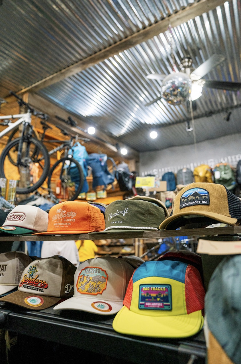 Shelf of Sendero and Cloudcroft New Mexico caps at High Altitude with mountain bikes hanging from the corrugated metal ceiling behind them