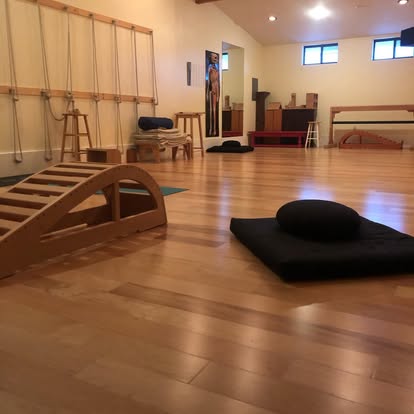 Yoga studio at Instant Karma with hardwood floor, ropes wall, wooden arch prop, meditation cushions, and a small altar