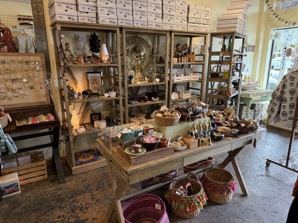 Statue and shelves at Instant Karma with Buddha and Hindu deity figures, candles, jewelry display, and hand-woven baskets