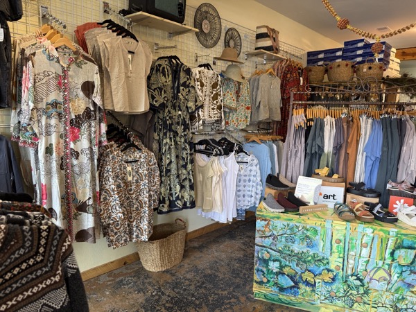 Boho clothing rack at Instant Karma with patterned dresses and tops, sun hats above, and Earth-brand sandals on a painted display