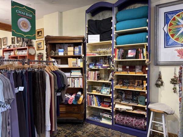 Chai Bar sign and yoga props at Instant Karma with stacked teal meditation cushions, drum, mala beads, and shelves of yoga books