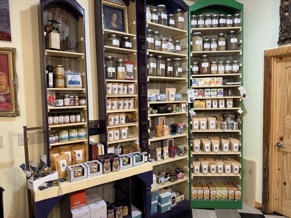 Apothecary wall at Instant Karma with shelves of glass jars holding bulk herbal teas and brown paper bags of loose leaf