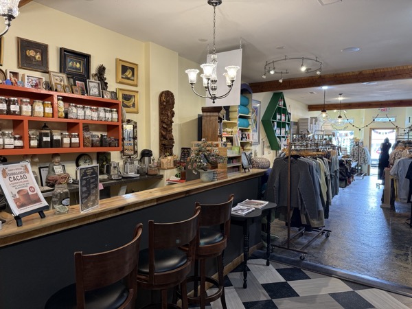 Chai bar at Instant Karma with bar stools, framed art, ceremonial cacao display, and clothing racks running back to the boutique