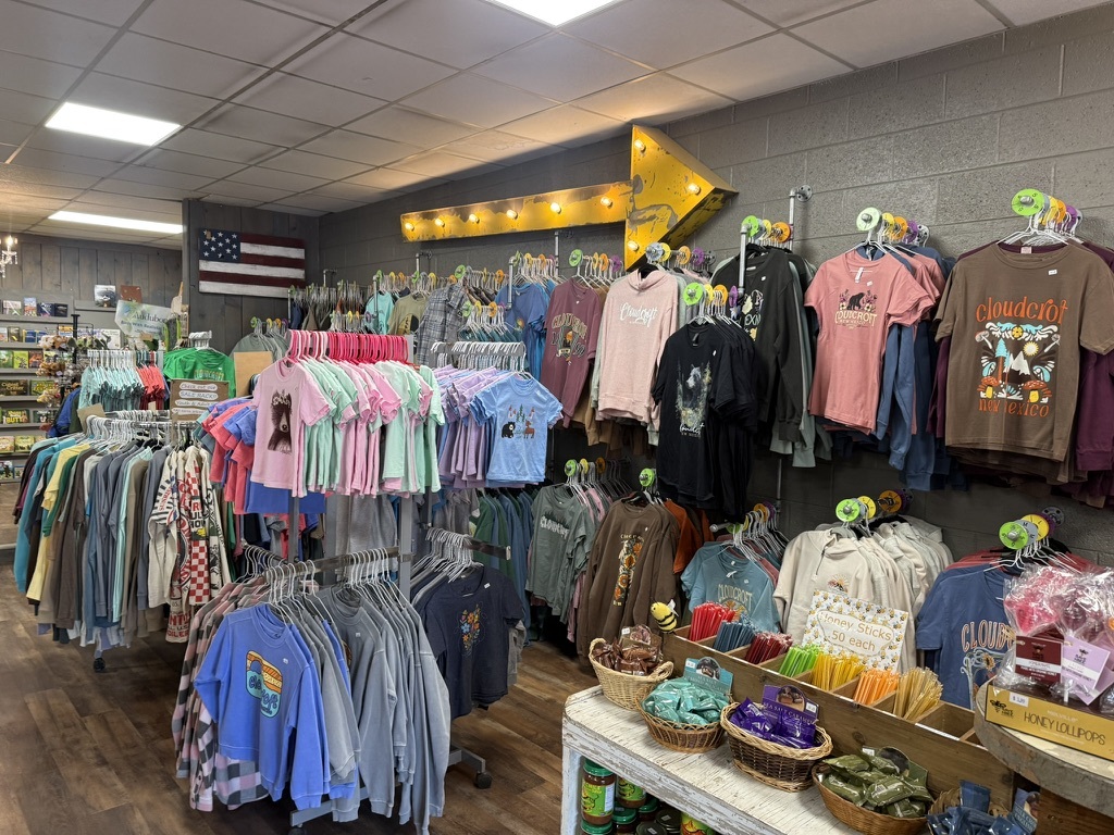 Wall of Cloudcroft-branded t-shirts and mountain-town apparel under a marquee arrow at Mountain Magic
