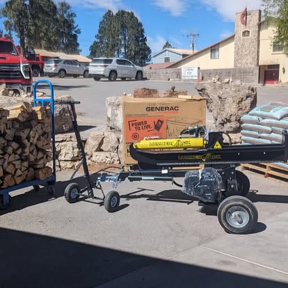 Generac generator and log splitter on display outside New Village Hardware with stacked firewood, a hand truck, and bagged goods
