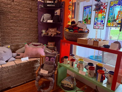 Interior corner with stuffed animals on shelves, a ceramic mug display, and stained-glass suncatchers in the window