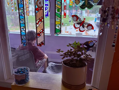 Window seat lined with stained-glass suncatchers and a butterfly piece, with a houseplant on the sill