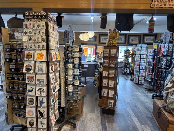 Sticker walls and Cloudcroft-themed merchandise at Poke The Bear with coasters, magnets, framed prints, and a lucky cat statue