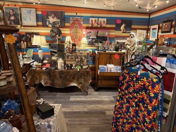 Vintage room corner at Poke The Bear with framed art including a Mona Lisa print, lamps, a hide-covered table, statue, and a colorful crocheted blanket on a rack