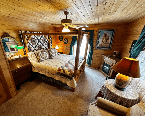 Guest room at Burro Street Boardinghouse with quilt-canopy king bed, wood-paneled walls, fireplace, and antique mirror