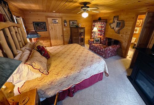 Texas Room at Burro Street Boardinghouse with log bed frame, Texas-themed wall art, quilt-covered bedding, and wood-paneled walls