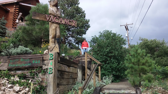 Burro Street Boardinghouse arrival — wood VACANCY sign with carved bear, painted Burro Street Boardinghouse sign, summer landscape