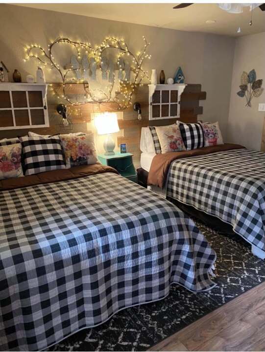 Themed motel room with twin beds, buffalo-check quilts, and twinkle-light branch headboard