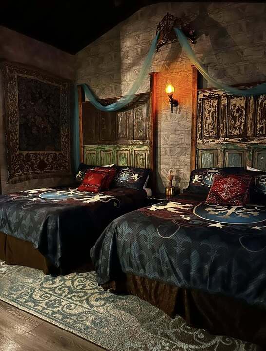 Medieval themed twin-bed room with carved wood headboards, sconce light, and cross-motif bedding